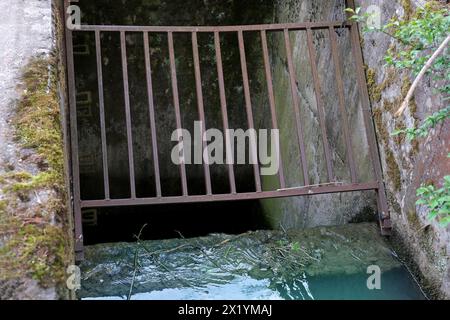 Griglia arrugginita di ferro da vicino di un pozzo di drenaggio dell'acqua, un torrente scorre in un canale, scarichi fognari, il concetto di un sistema di drenaggio in Europa, un fiume dra Foto Stock