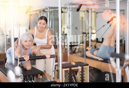 Donna anziana che fa pilates sul riformatore con una giovane addestratrice Foto Stock