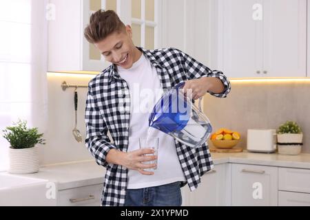 Uomo felice che versa acqua dalla caraffa del filtro in vetro in cucina Foto Stock