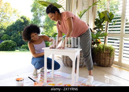 Madre birazziale e figlia adulta dipingono mobili fuori casa in un progetto di upcycling Foto Stock