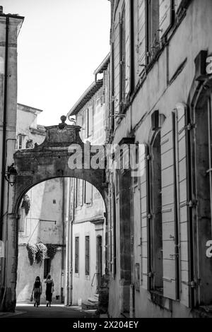 Due donne che camminano attraverso un cancello ad arco in pietra nella città medievale di Arles, in Francia Foto Stock