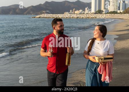 Una coppia gode di un brindisi al tramonto sulla spiaggia con una bottiglia di vino e spuntini Foto Stock