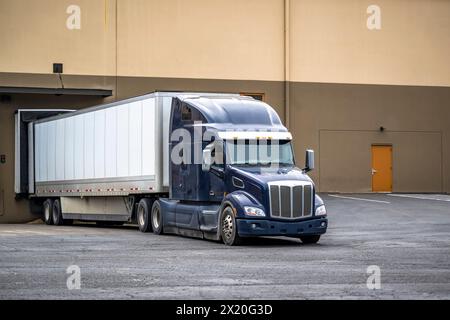Autocarro lungo standard industriale blu con semirimorchio per furgoni a secco in piedi sui cancelli di carico del carico commerciale per il trasporto di merci commerciali Foto Stock