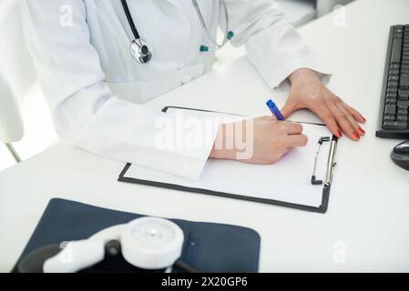 Un esperto medico si concentra sulla scrittura delle informazioni vitali in un ambiente clinico. Foto Stock