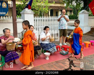 Luang Prabang, Laos. 16 aprile 2024. Due giovani novizi in abiti arancioni ricevono cibo durante le elemosine mattutine nella vecchia città reale di Luang Prabang. E' un antico rituale. L'affascinante spettacolo attira ora sempre più turisti da tutto il mondo. Crediti: Carola Frentzen/dpa/Alamy Live News Foto Stock