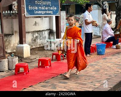 Luang Prabang, Laos. 16 aprile 2024. Un giovane novizio in una veste arancione durante la mattinata di elemosina nella vecchia città reale di Luang Prabang. E' un antico rituale. L'affascinante spettacolo attira ora sempre più turisti da tutto il mondo. Crediti: Carola Frentzen/dpa/Alamy Live News Foto Stock