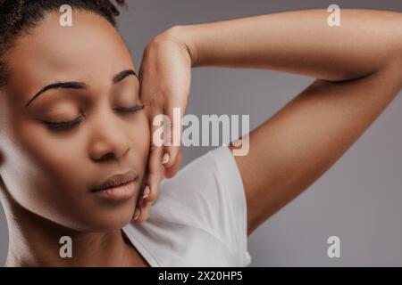 La giovane donna nera trasuda tranquillità con gli occhi chiusi, la mano sulla guancia Foto Stock