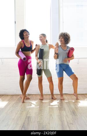 Tre donne diverse stanno ridendo insieme in un luminoso studio di yoga, spazio copia Foto Stock