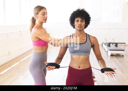 Donna caucasica che regola la postura della donna birazziale nello studio di pilates riformatori Foto Stock