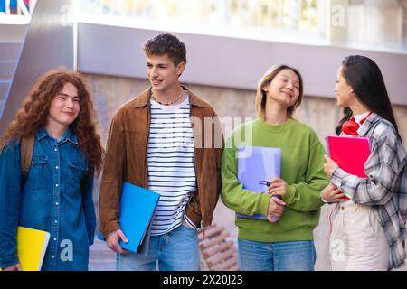 Gruppo multirazziale di studenti felici e sorridenti con quaderni in mano a camminare . Foto Stock