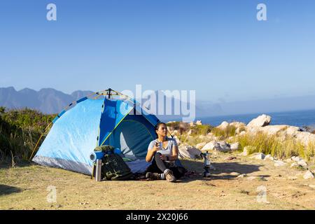 Escursionista birazziale seduto vicino alla tenda, guardando lontano, copia spazio Foto Stock