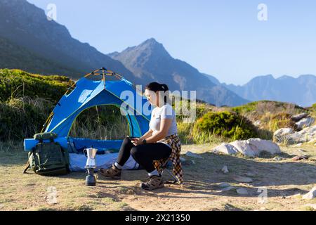 Escursionista birazziale seduto accanto alla tenda, preparando il caffè, copiando lo spazio Foto Stock