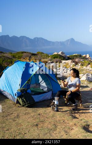 Escursionista birazziale seduto accanto alla tenda, con smartphone, spazio fotocopie Foto Stock