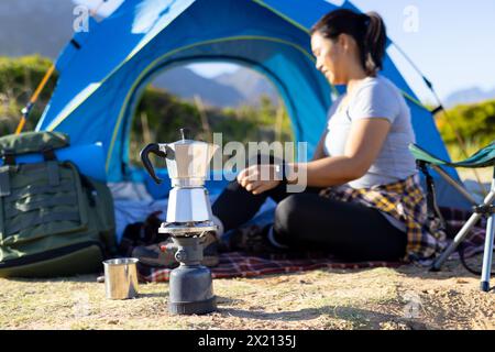 Escursionista birazziale seduto vicino alla tenda, che prepara caffè Foto Stock