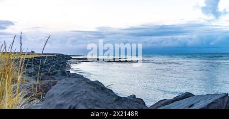 Una costa rocciosa con un corpo d'acqua sullo sfondo. Il cielo è nuvoloso e l'acqua è calma Foto Stock