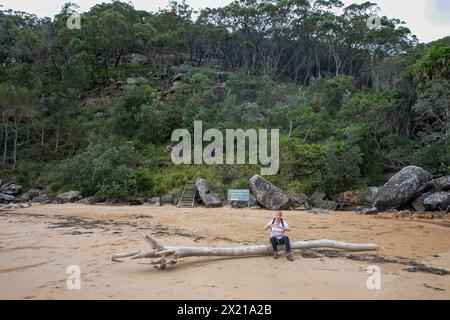 Resolute Beach, donna di mezza età si riposa su un pezzo di driftwood, parco nazionale di caccia Ku-ring-GAI, NSW, Australia, 2024 Foto Stock