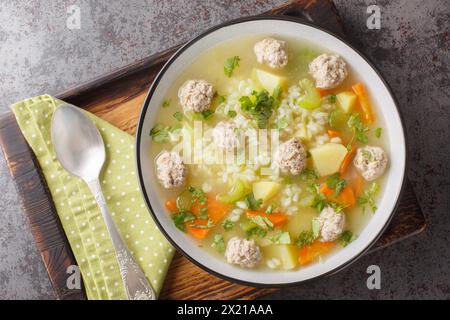 Zuppa dietetica di polpette di riso con sedano, carote, cipolle, patate ed erbe aromatiche da vicino in un recipiente sul tavolo. Vista dall'alto orizzontale Foto Stock