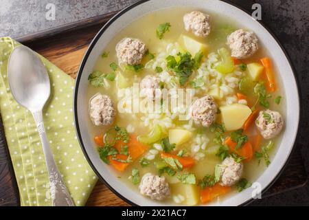 Zuppa calda di polpette di riso fatta in casa con sedano, carote, cipolle e patate da vicino in un recipiente sul tavolo. Vista dall'alto orizzontale Foto Stock