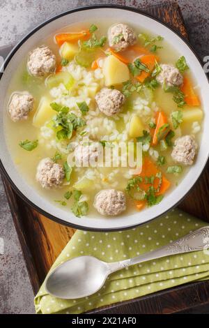 Zuppa di riso con polpette, verdure ed erbe aromatiche da vicino in una ciotola sul tavolo. Vista dall'alto verticale Foto Stock