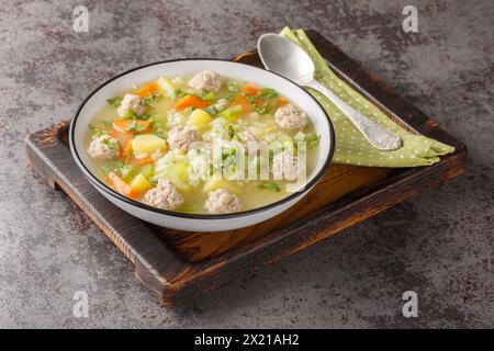 Deliziosa zuppa di riso con polpette, sedano, carote, cipolle, patate ed erbe aromatiche da vicino in un recipiente sul tavolo. Orizzontale Foto Stock