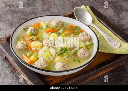 Zuppa dietetica di polpette di riso con sedano, carote, cipolle, patate ed erbe aromatiche da vicino in un recipiente sul tavolo. Orizzontale Foto Stock