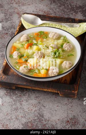 Zuppa di riso con polpette di sedano, carote, cipolle e patate da vicino in un recipiente sul tavolo. Verticale Foto Stock