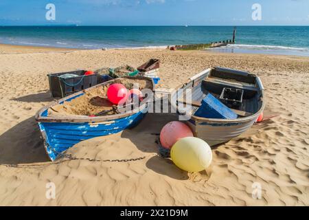 Branksome Dene Beach, Bournemouth, Regno Unito - 6 ottobre 2023: Due barche a remi, una piene di sabbia accanto a reti da pesca, su una spiaggia sabbiosa vuota. Foto Stock