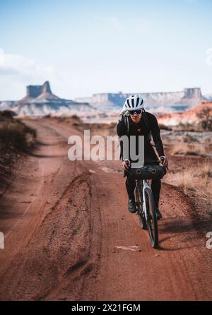 Un ciclista maschile corre lungo la remota strada desertica a Canyonlands, Utah Foto Stock