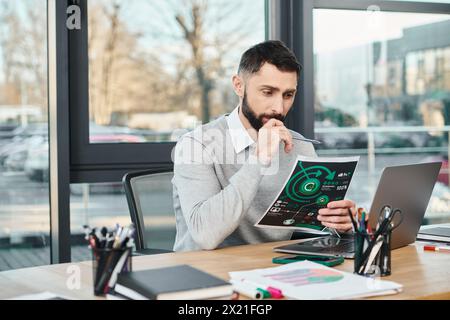 Un uomo siede a una scrivania, profondamente impegnato in grafici, assorbito nell'apprendimento e nella riflessione. Foto Stock