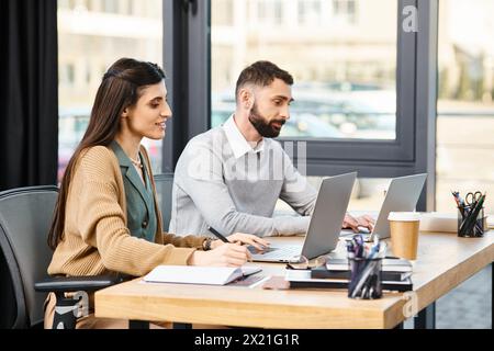 Due professionisti si siedono a un tavolo in ufficio, impegnati a lavorare sui loro computer portatili, mostrando una cultura aziendale moderna. Foto Stock