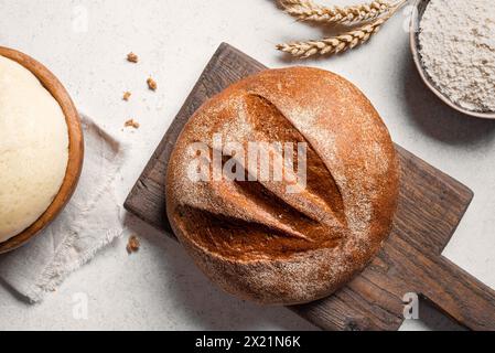 Pane e ingredienti freschi a base di lievito madre. Pagnotta di pane sul tagliere, palla di impasto e farina sul tavolo bianco, fondo cottura. Foto Stock