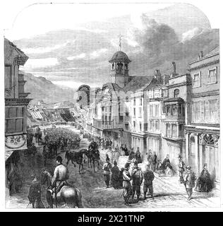 The Volunteer Review: The High-Street of Guildford on Easter Sunday, 1864. "La città è costituita principalmente da questa strada principale, che corre lungo la ripida collina sulla riva orientale del fiume Wey. Ci sono pochi esemplari migliori di una vecchia città di campagna inglese di questa piccola capitale rustica del Surrey... la Guildhall, costruita all'epoca di Carlo II... si distingue all'esterno per il suo orologio a proiezione, con nodi e decorazioni di ferro dorato. Tale è la città di Guildford, che dal venerdì Santo al lunedì di Pasqua quest'anno è stata affollata di visitatori di vacanza ben al di là della sua capacità Foto Stock