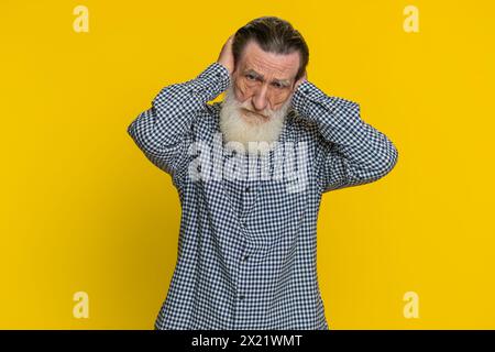 Non voglio sentire e ascoltare. Frustrato infastidito irritato anziano che copre le orecchie gestendo di no, evitando consigli ignorando rumori sgradevoli voci forti. Nonno isolato su sfondo giallo Foto Stock