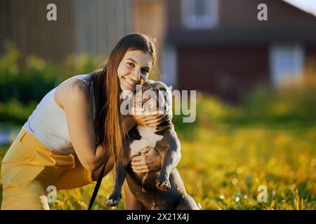 La giovane donna ha sollevato la museruola del bullo americano per fare un ritratto congiunto con il suo cane, la donna bianca viene fotografata con il suo animale domestico la sera d'estate sul prato. Foto Stock