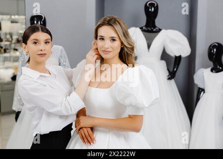 La futura sposa è venuta in un salone di abiti da sposa per comprare un abito. Una bella donna sceglie un abito da sposa nel salone, e un assistente aiuta la sposa Foto Stock