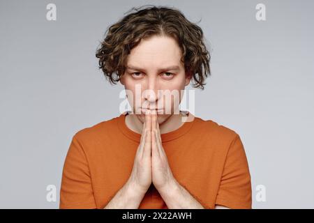Ritratto in studio del giovane uomo caucasico che si sente in colpa posare per la macchina fotografica con le mani di preghiera, copia spazio Foto Stock