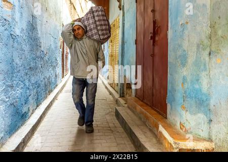 Un portiere sta camminando lungo un vicolo stretto nella medina di Fez, in Marocco. Foto Stock