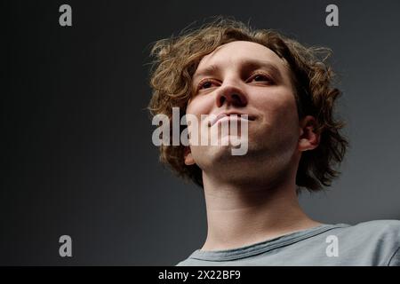 Primo piano ad angolo basso di un giovane uomo caucasico sicuro di sé con capelli ricci sorrisi, copia spazio Foto Stock