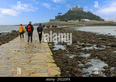 Turisti che camminano sulla strada rialzata delle maree fino a St Michael's Mount, un'isola di marea nella Baia di Mount, Marazion, Penzance, Cornovaglia, Inghilterra, Regno Unito Foto Stock