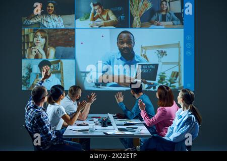 I lavoratori seduti a un tavolo nella sala riunioni partecipano a una riunione virtuale, tenendo una lezione di inglese aziendale online con il tutor Foto Stock