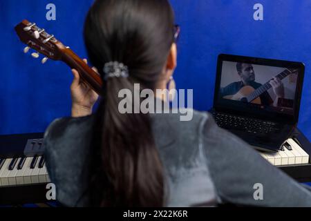 Un giovane insegnante latinoamericano insegna la chitarra online utilizzando un computer portatile. Concetto di lezioni di musica a distanza Foto Stock