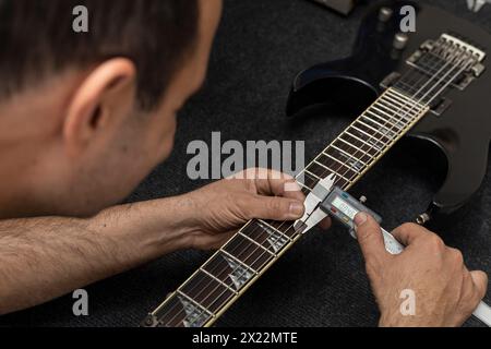 Il liutaio latinoamericano calibra le corde di una chitarra elettrica con un calibro digitale. Irriconoscibile. Concetto di chitarra, calibrazione, strumento. Foto Stock