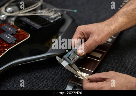 Il liutaio latinoamericano misura lo spessore di un capo di basso elettrico con un calibro digitale. Irriconoscibile. Concetto bassi, calibrazione, strumento. Foto Stock