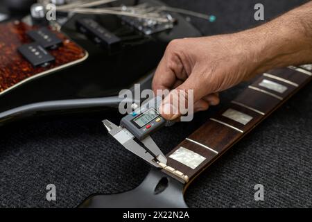 Il liutaio latinoamericano misura lo spessore di un capo di basso elettrico con un calibro digitale. Irriconoscibile. Concetto bassi, calibrazione, strumento. Foto Stock