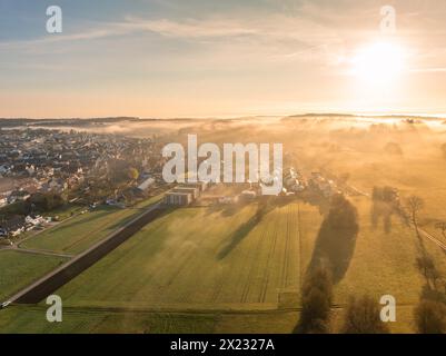 Alba dietro una piccola città con nebbia sui campi in primo piano, Gechingen, Foresta Nera, Germania Foto Stock