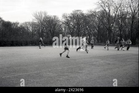 Anni '1970, un gruppo di scolari che giocano a football all'aperto in un grande parco giochi scolastico, Inghilterra, Regno Unito. Foto Stock