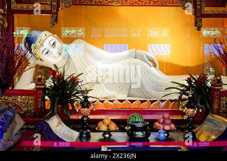 Buddha di Giada reclinabile, Tempio del Buddha di Giada, Shanghai, Buddha all'altare circondato da offerte e decorazioni floreali in un'atmosfera tranquilla, Shanghai Foto Stock