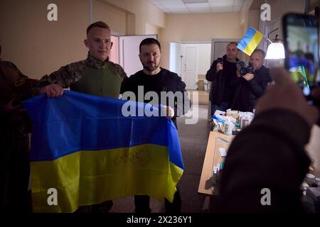 Slovyansk, Ucraina. 19 aprile 2024. Il presidente ucraino Volodymyr Zelenskyy, a destra, posa con un soldato che detiene una bandiera Ucraina autografata durante una visita a un ospedale militare nella regione del Donbas, 19 aprile 2023 a Slovyansk, Oblast di Donetsk, Ucraina. Credito: Handout/Ufficio stampa presidenziale ucraino/Alamy Live News Foto Stock