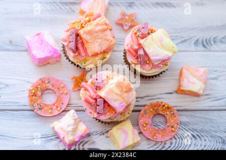 Cupcake rosa color pastello con cioccolato, ciambelle e marshmallow arcobaleno Foto Stock