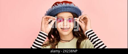 Un'elegante ragazza adolescente indossa con sicurezza un abbigliamento vivace, con un cappello e occhiali da sole alla moda. Foto Stock